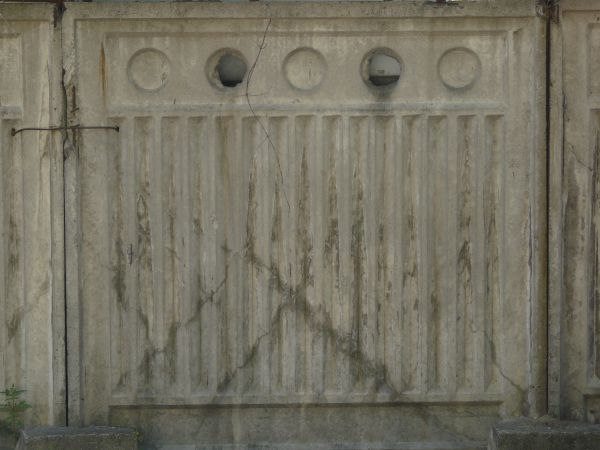 Concrete fence texture molded with a pattern of circles above vertical recessions, with large cracks and stains. The fence appears to be crumbling around the edges.